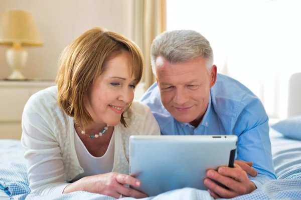 Gülümseyen Olgun Çift Evde Yatarken Dijital Tableti Paylaşıyor — Stok fotoğraf