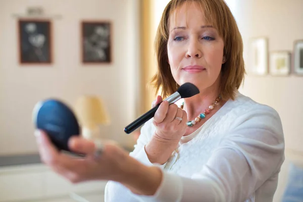 Mature woman applying makeup while standing in bedroom — Stock Photo, Image