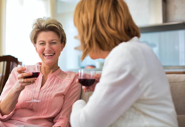 Reife Frauen trinken Wein, während sie zu Hause auf dem Sofa sitzen — Stockfoto