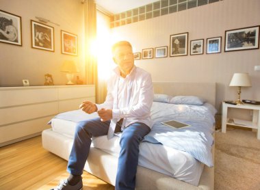 Üst düzey bir adam işe hazırlanıyor. Yatak odasında gömlek ve kravat giyiyor.