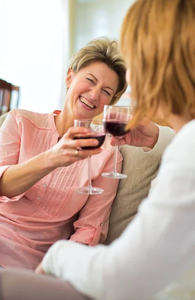 Зрелые женщины пьют вино, сидя дома на диване — стоковое фото