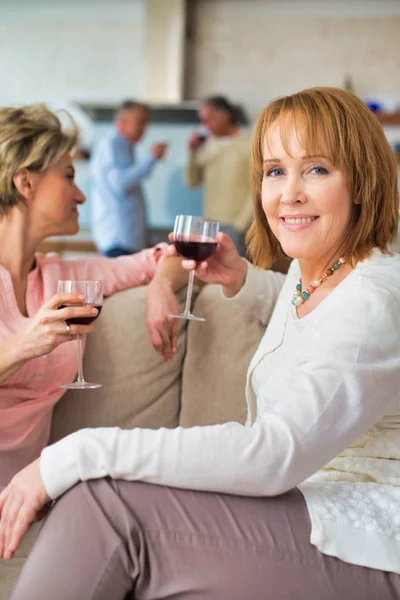 Volwassen vrouwen die wijn drinken terwijl ze thuis op de bank zitten — Stockfoto