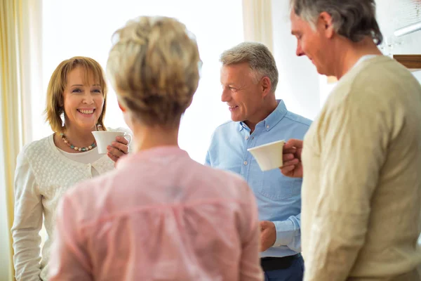 Lächelnde ältere Freunde halten Getränke in der Hand, während sie im Wohnzimmer reden — Stockfoto
