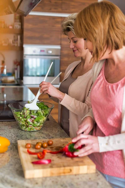 Glimlachende volwassen vrienden bereiden maaltijd in de keuken — Stockfoto