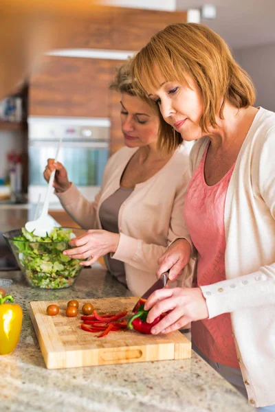 Glimlachende volwassen vrienden bereiden maaltijd in de keuken — Stockfoto