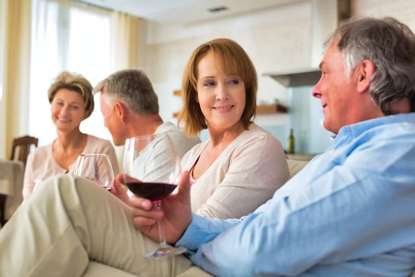 Starší přátelé držící sklenice na víno v obývacím pokoji — Stock fotografie
