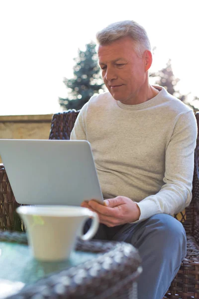 Olgun adam verandada hasır sandalyede otururken dizüstü bilgisayar kullanıyor. — Stok fotoğraf