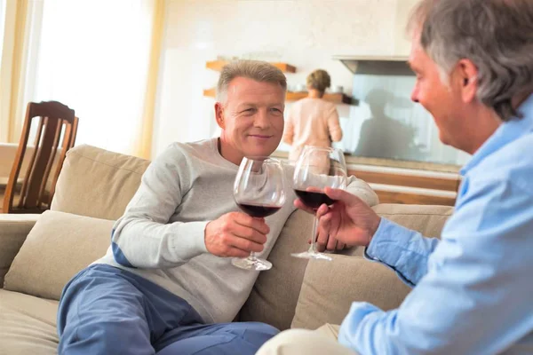 Mature friends drinking wine while sitting on sofa