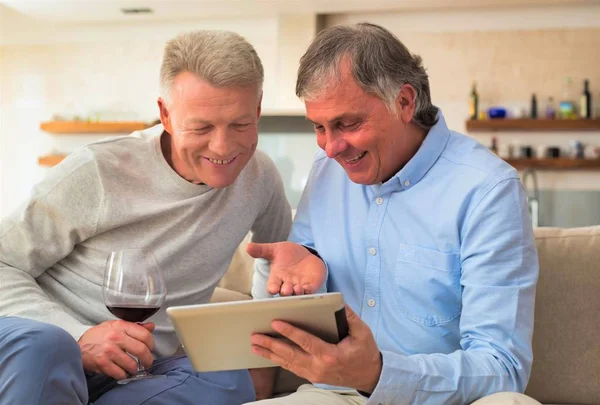 Χαμογελώντας ώριμοι άνδρες χρησιμοποιώντας ψηφιακή ταμπλέτα, ενώ κάθεται στο σπίτι — Φωτογραφία Αρχείου