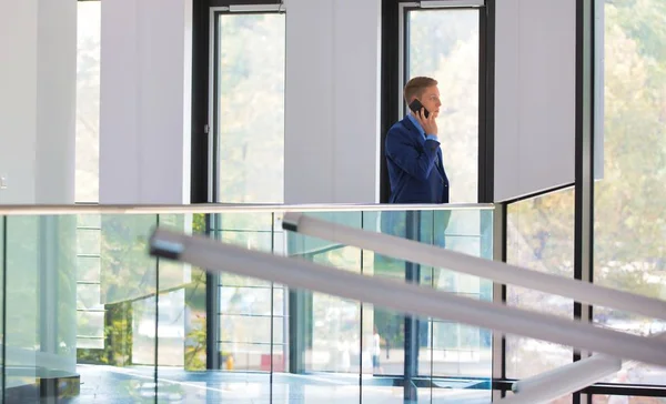 オフィスで手すりに立ちながらスマート フォンで話している青年実業家 — ストック写真
