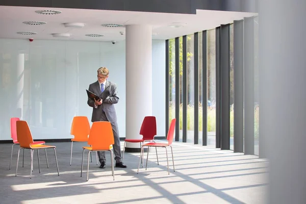 Olgun Işadamı Yeni Ofiste Sandalyelerin Ortasında Dururken Belge Okuyor — Stok fotoğraf