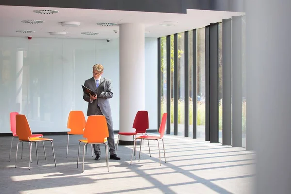 Mature Businessman Reading Document While Standing Amidst Chairs New Office — Stock Photo, Image