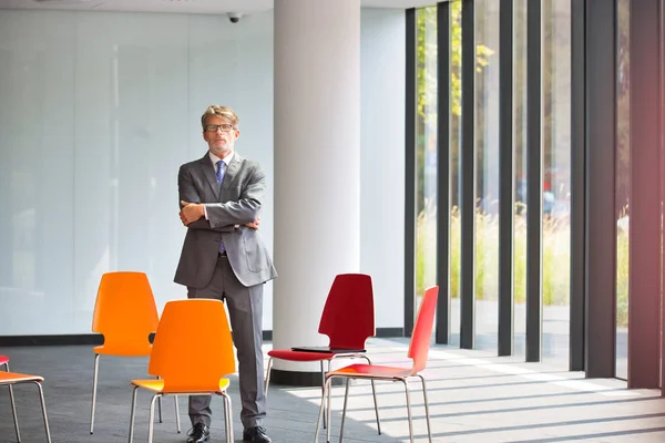 Confident Mature Businessman Standing Arms Crossed Amidst Chairs New Office — Stock Photo, Image