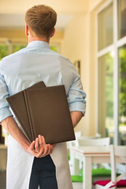 Genç garson menüler dururken restoranda holding arka görünümü