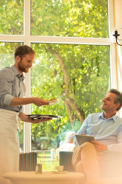 Young Waiter Serving Coffee Food While Mature Customer Using Digital — Stock Photo, Image