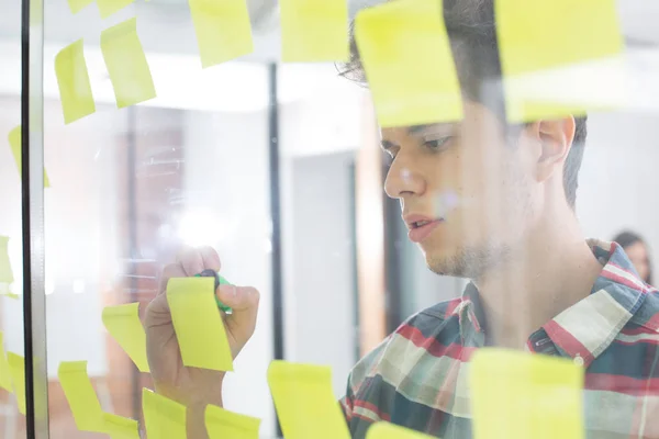 Young businessman writing on sticky notes in office — Stock Photo, Image