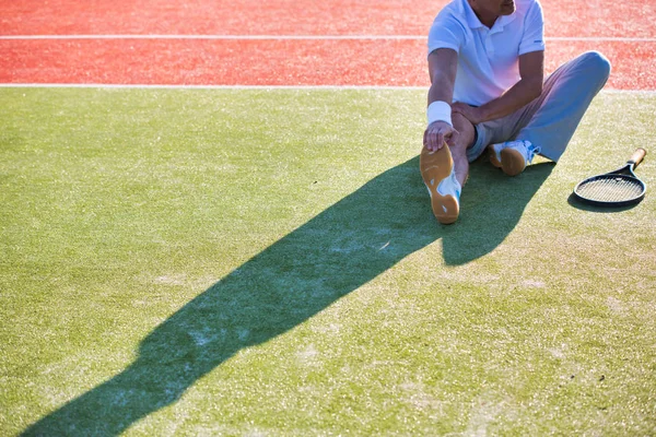 Dojrzały mężczyzna rozgrzewa się podczas rozciągania na korcie tenisowym — Zdjęcie stockowe