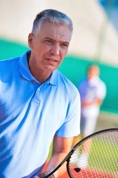 Зрілий чоловік тримає тенісну ракетку проти друга, граючи матч на — стокове фото