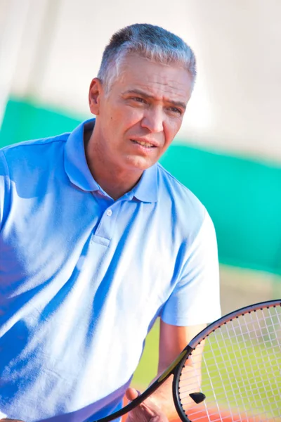 Mature man holding tennis racket against friend playing match on — ストック写真