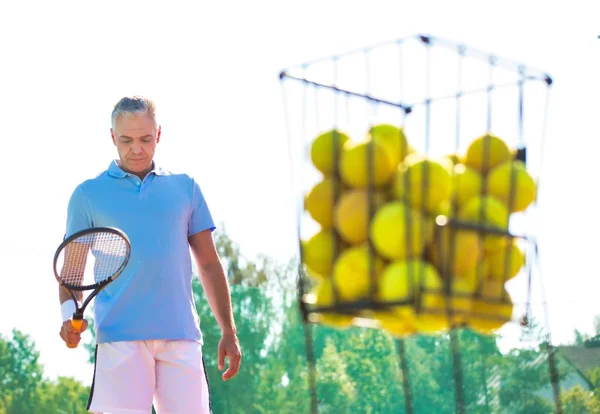 Olgun bir adam tenis raketini taşaklarında tutarken yürüyor. — Stok fotoğraf