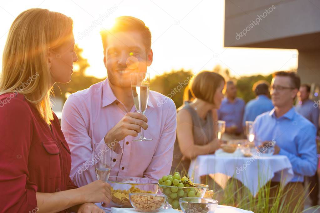 Business People enjoying a Successful summertime roof party for either a business conference after party, a convention drinks, a wedding, a birthday party or a family reunion or anniversary with a strong lens flare whilst having a toast