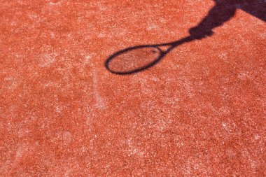Olgun bir adamın gölgesi tenis topuna kırmızı cour ile vuruyor.