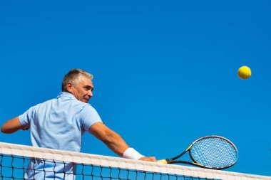 Düşük açılı görünümü ile raket açık mavi gökyüzü karşı kortta tenis topu isabet emin olgun adam