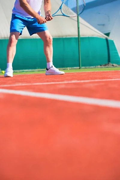 Homem maduro confiante batendo bola de tênis com raquete na pele vermelha — Fotografia de Stock