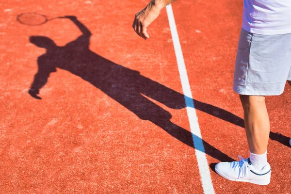 Schatten eines reifen Mannes schlägt Tennisball mit Schläger auf rotem Grund — Stockfoto