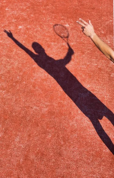 Schatten eines reifen Mannes schlägt Tennisball mit Schläger auf rotem Grund — Stockfoto