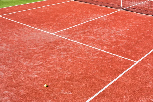 Tennis ball on red court during sunny day — Stock Photo, Image