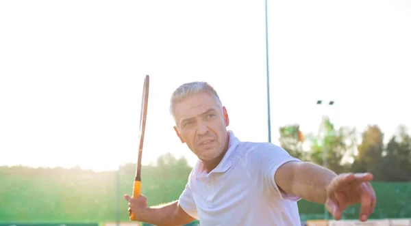 Olgun adam güneşli bir günde tenis topuna vuruyor. — Stok fotoğraf