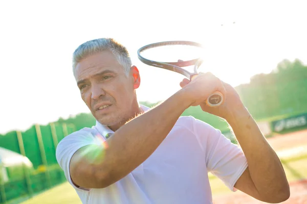 Olgun adam güneşli bir günde tenis topuna vuruyor. — Stok fotoğraf