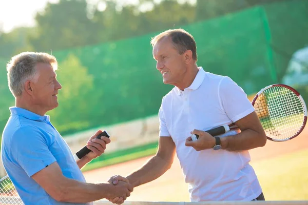 Men shaking hands while standing at tennis court against clear s — ストック写真
