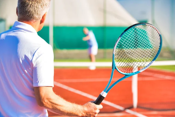 Aktivní senioři hrají tenis za slunečného dne na červeném kurtu — Stock fotografie