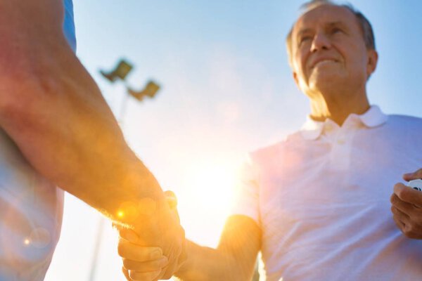 Smiling mature tennis player shakes hand after finishing game