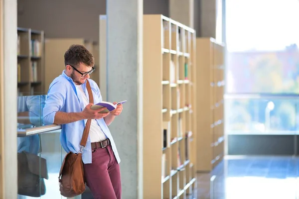 Ung student läser bok när du står vid räcke i korridoren — Stockfoto