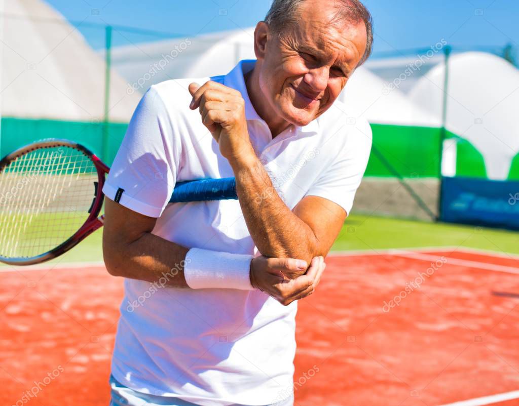 Senior man with elbow pain standing during tennis match on sunny