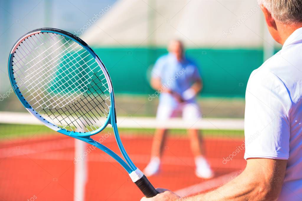 Active seniors playing tennis on sunny day at red court