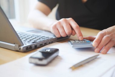 Ön planda dizüstü bilgisayarı cep telefonu ve kalemle orta kısımda hesap makinesi kullanan adam.