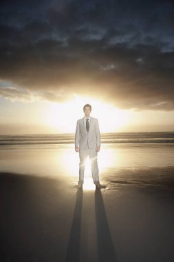 Business man standing on beach against sunset portrait clipart