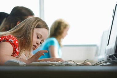 Down sendromlu kız (10-12) bilgisayar laboratuarındaki çocukların arka planında bilgisayar kullanıyor