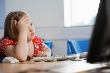 Girl (10-12) with Down syndrome sitting in computer lab clipart