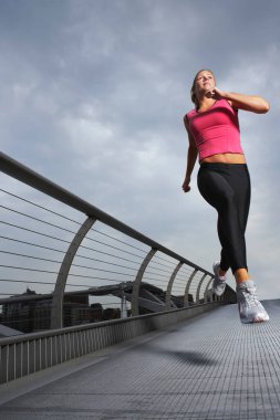 Woman jogging on foot bridge low angle view Millennium Bridge London England clipart