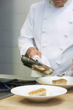 Erkek aşçı elinde tavayla mutfaktaki tabaklara yemek servisi yapıyor.