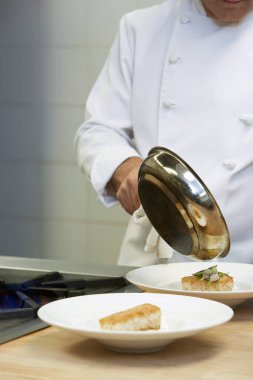 Erkek aşçı elinde tavayla mutfaktaki tabaklara yemek servisi yapıyor.