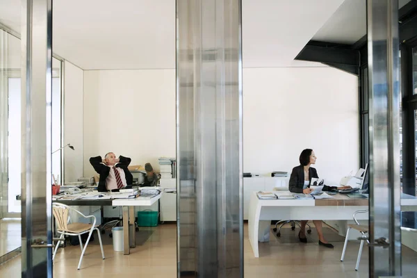 Vista Através Portas Transparentes Empresária Trabalhando Escritório Enquanto Empresário Relaxa — Fotografia de Stock