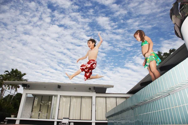 Boy (7-9) jumping into pool girl (5-6) watching