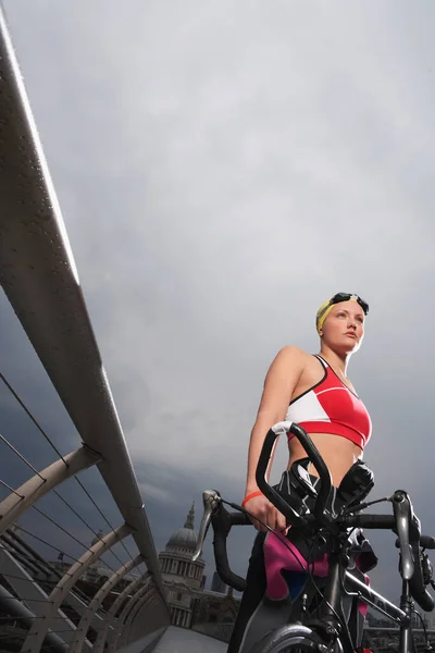 三项全能运动员骑着自行车站在人行天桥上低角度俯瞰伦敦千禧桥 — 图库照片