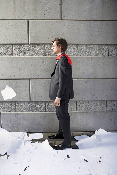 Деловой человек в окружении бумажного материала у стены